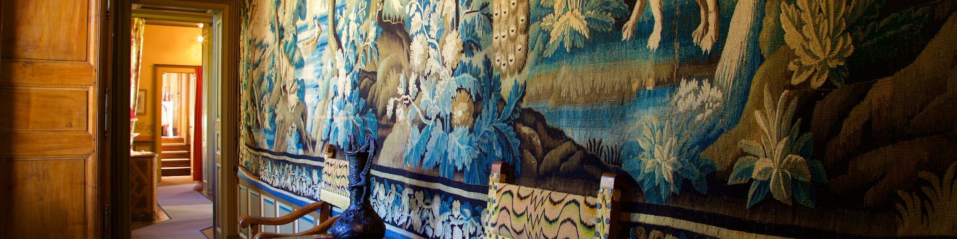 A hallway with a large tapestry depicting a lion and other animals, wooden furniture, and a patterned rug.