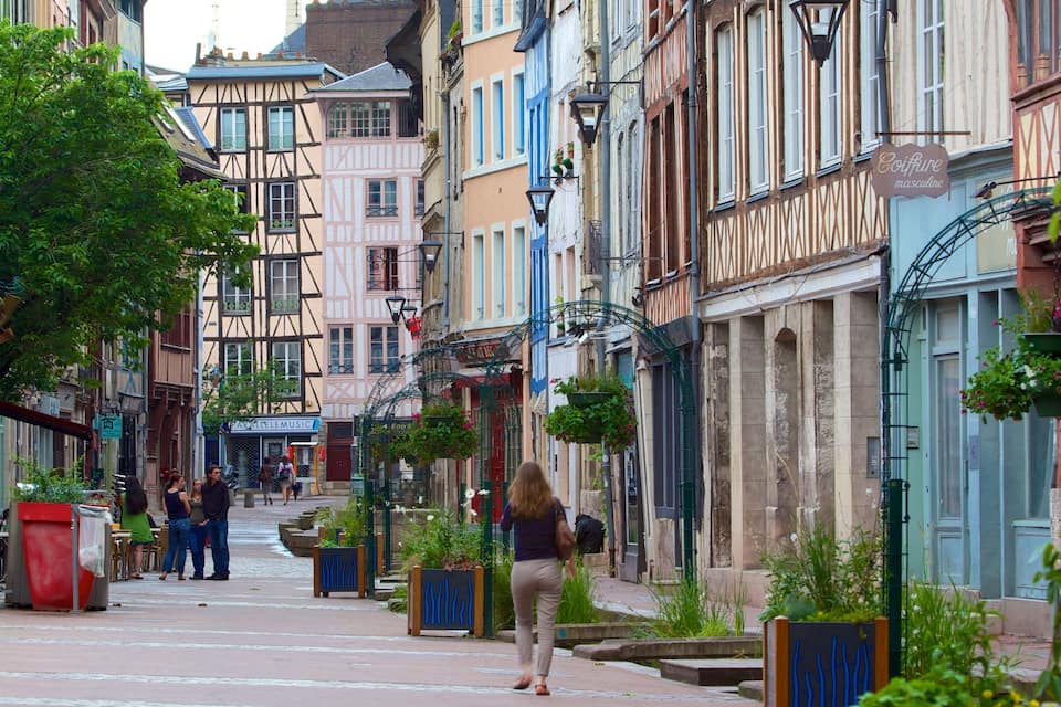 A narrow street lined with colorful half-timbered buildings, a café, and hanging flower baskets.