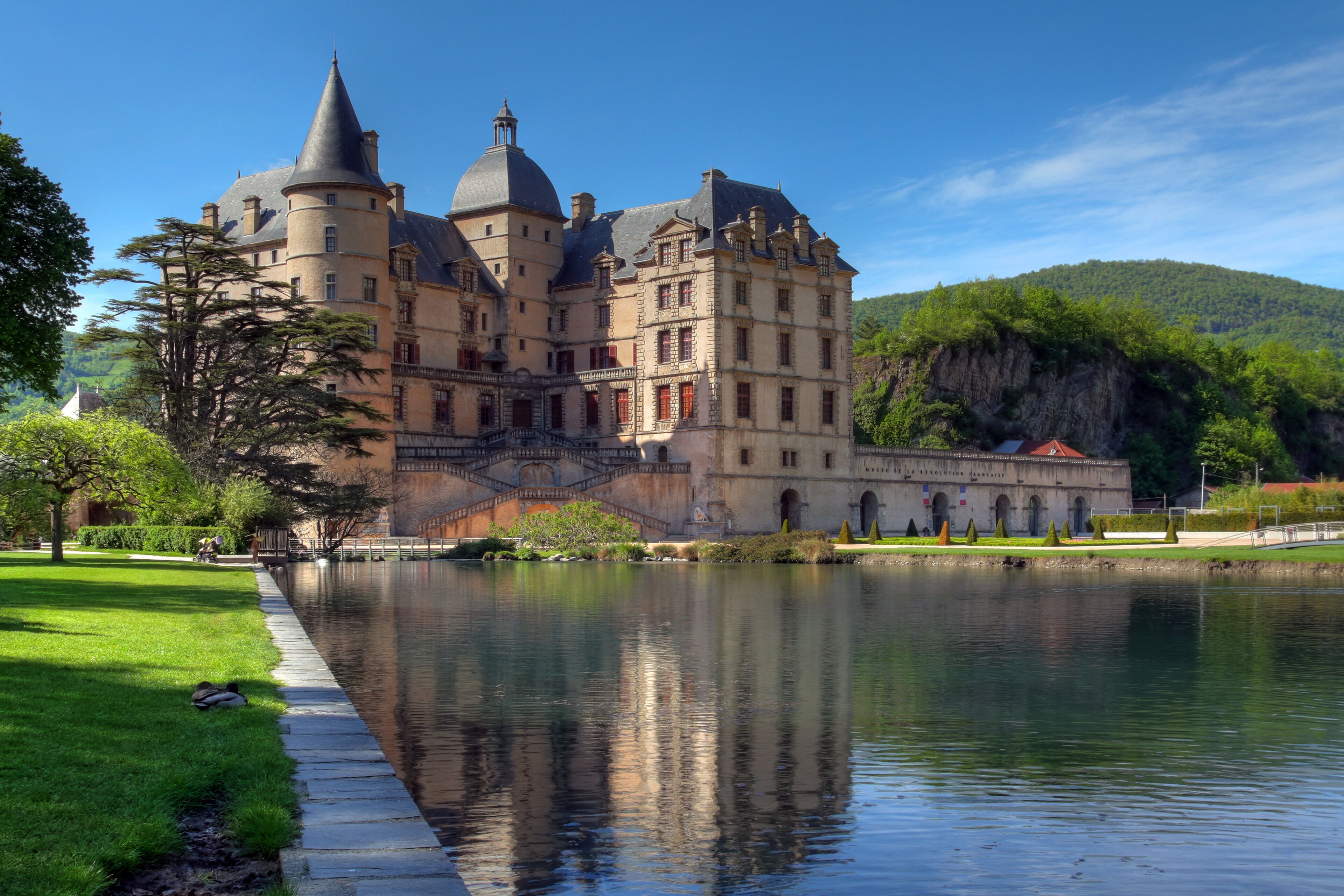 A historic castle with multiple towers, a moat, and lush greenery.