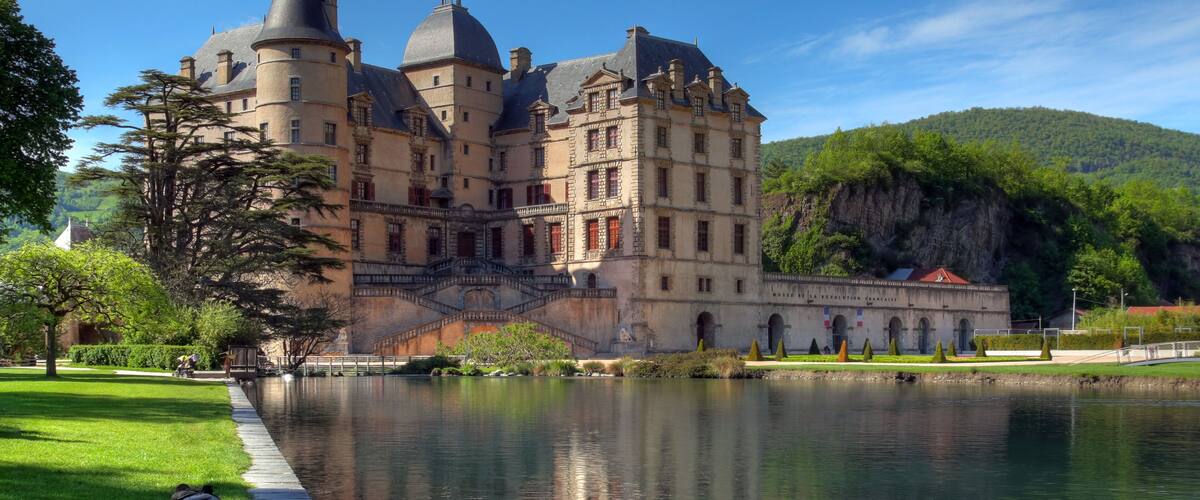 A historic castle with multiple towers, a moat, and lush greenery.