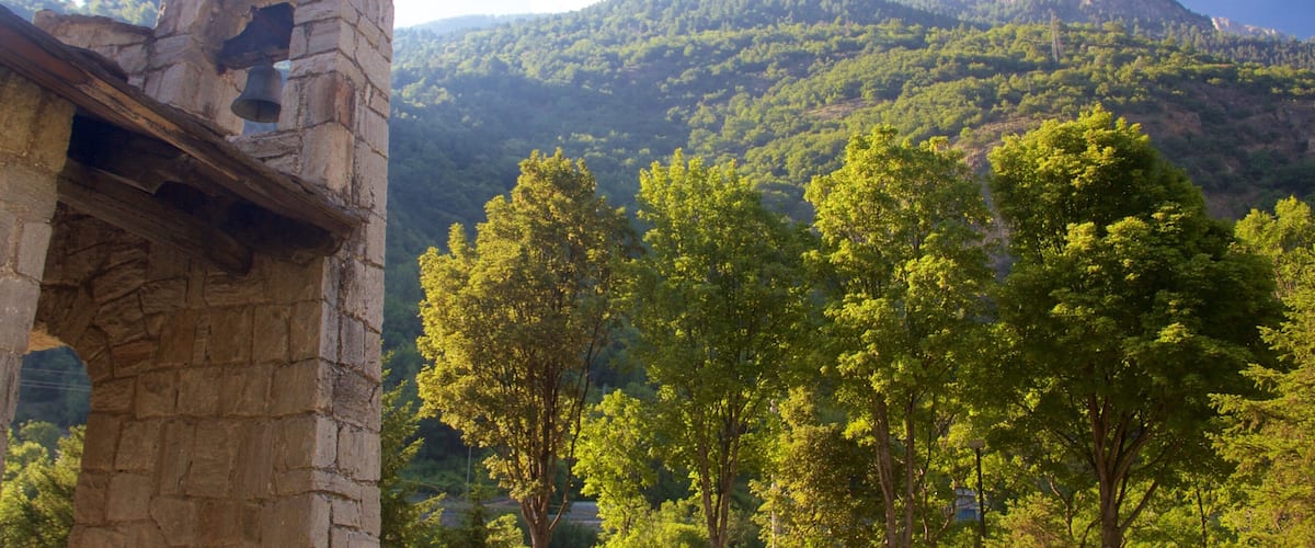A stone tower with a bell, surrounded by lush green trees and a mountain in the background.