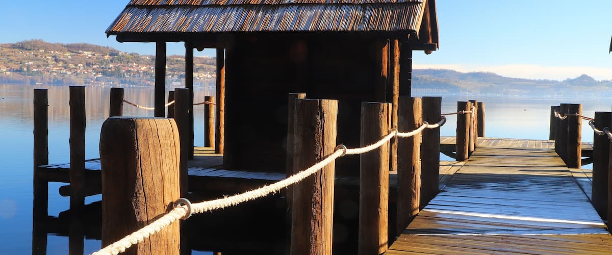 A wooden dock with a small hut at the end, leading into calm water with a distant shoreline.