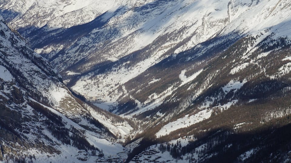 A snow-covered mountain range with a valley and a small settlement.