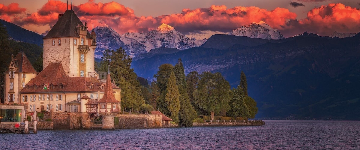 A castle by a lake with mountains in the background.
