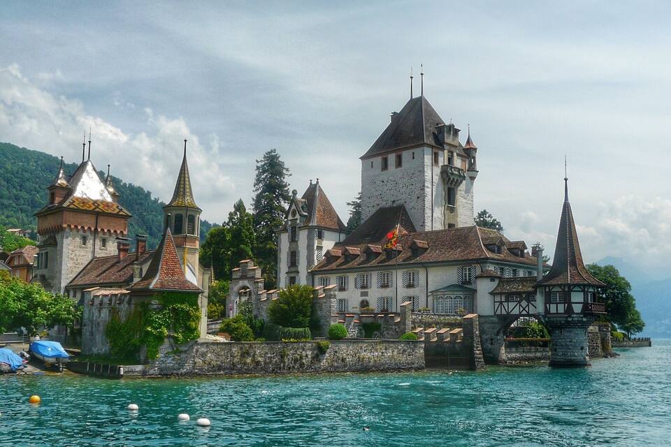 A historic castle with towers and a tower with a spire, surrounded by water and greenery.