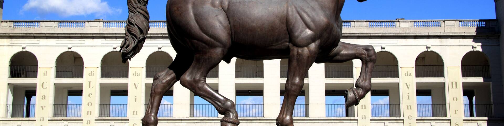 Una estatua de bronce de un caballo frente a un edificio con ventanas arqueadas y columnas.
