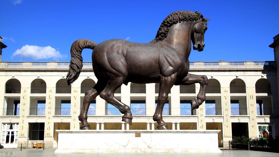 A bronze horse statue in front of a building with arched windows and columns.