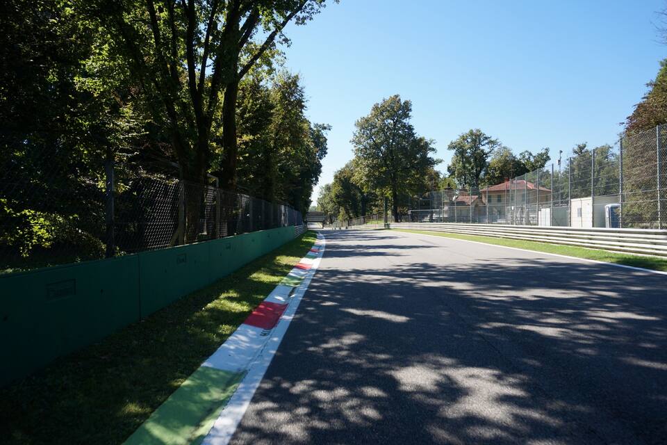 A racetrack with a green safety fence, trees, and a clear sky.