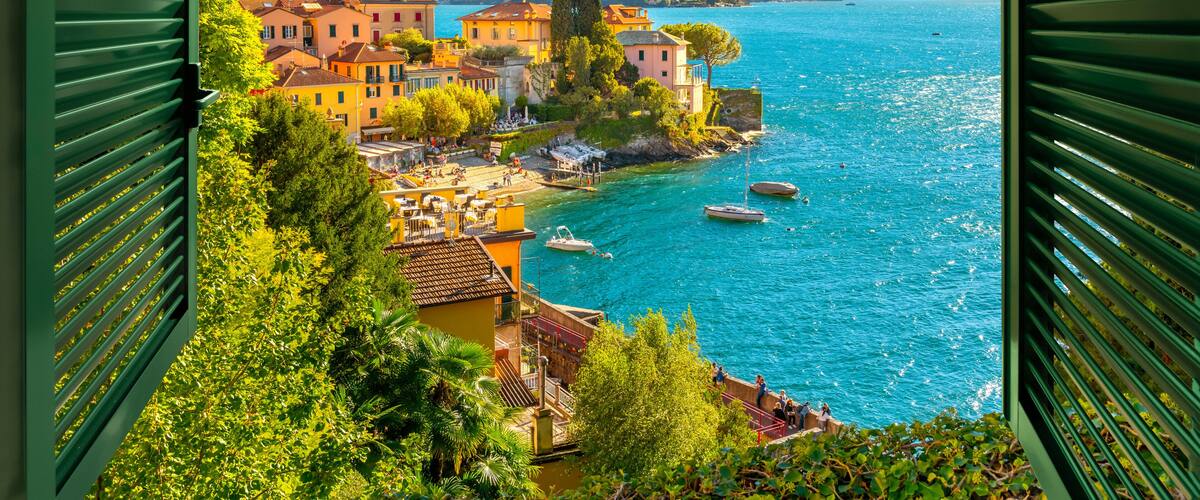 View through an open window with shutters looking down on the colorful picturesque village of Varenna, Italy, on the shores of Lake Como at summer.