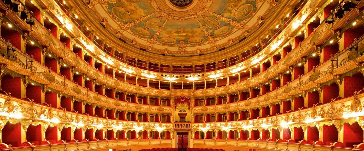 An ornate theater with red velvet seats and a grand, decorated ceiling.
