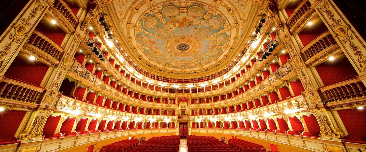 An ornate theater with a grand, circular ceiling and red velvet seats.