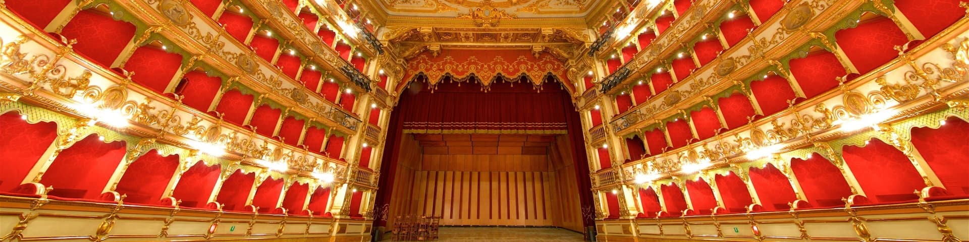 An ornate theater interior with red seats, a central stage, and a detailed ceiling.