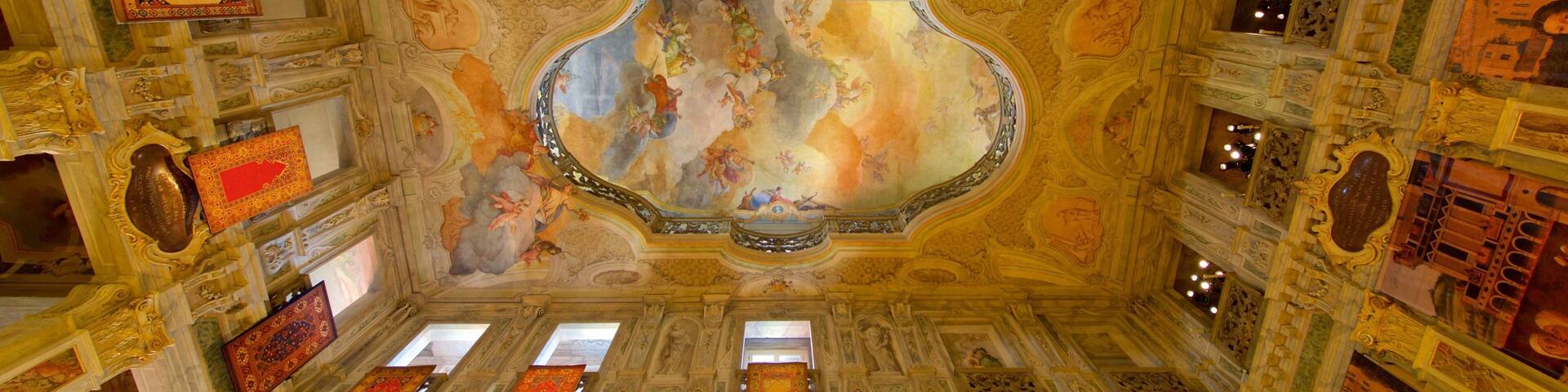 An ornate room with elaborate ceiling frescoes, golden chandeliers, and intricate wall decorations.