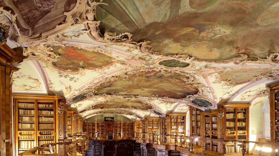 An ornate library with elaborate ceiling frescoes and tall bookshelves filled with books.