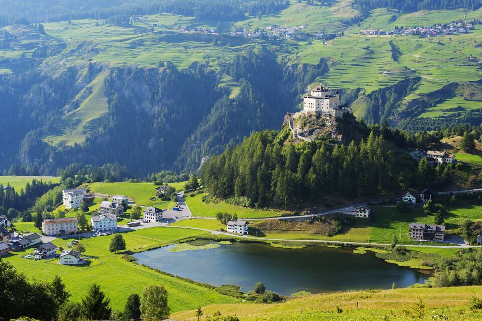 A castle on a hill overlooking a town and a lake.