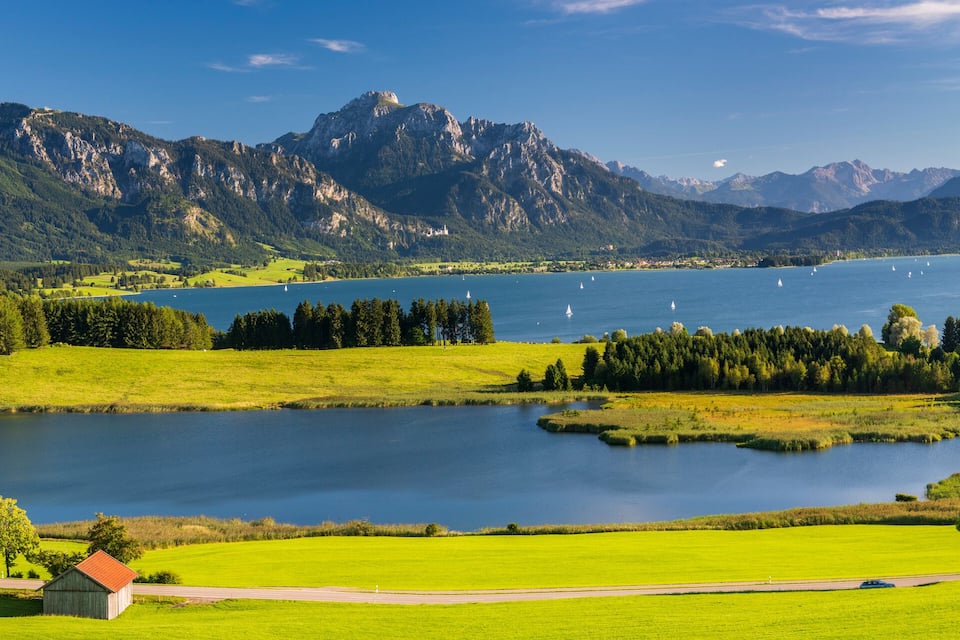 A lake surrounded by mountains, a small house, and a road.
