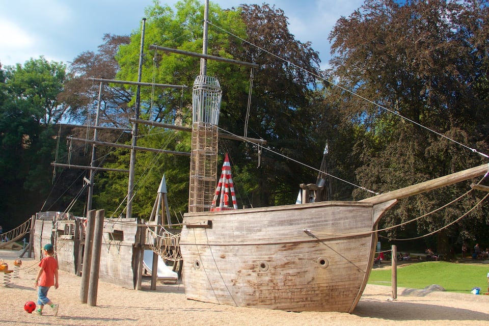 A wooden pirate ship model with ropes and a lifeboat in a park.