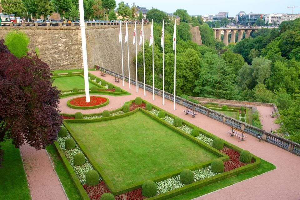 Un jardin bien entretenu, avec une pelouse centrale, des parterres de fleurs et un mât pour drapeau.