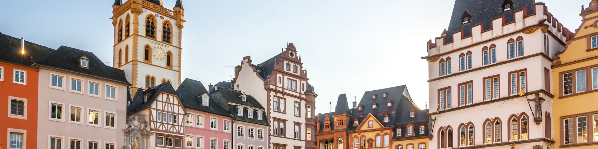 Uma praça de paralelepípedos com edifícios históricos, uma torre do relógio imponente e cafés ao ar livre.