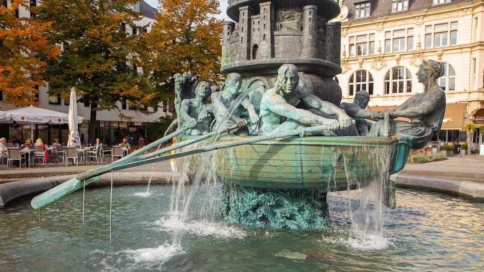 A bronze statue of rowers in a boat, surrounded by water, with a building in the background.