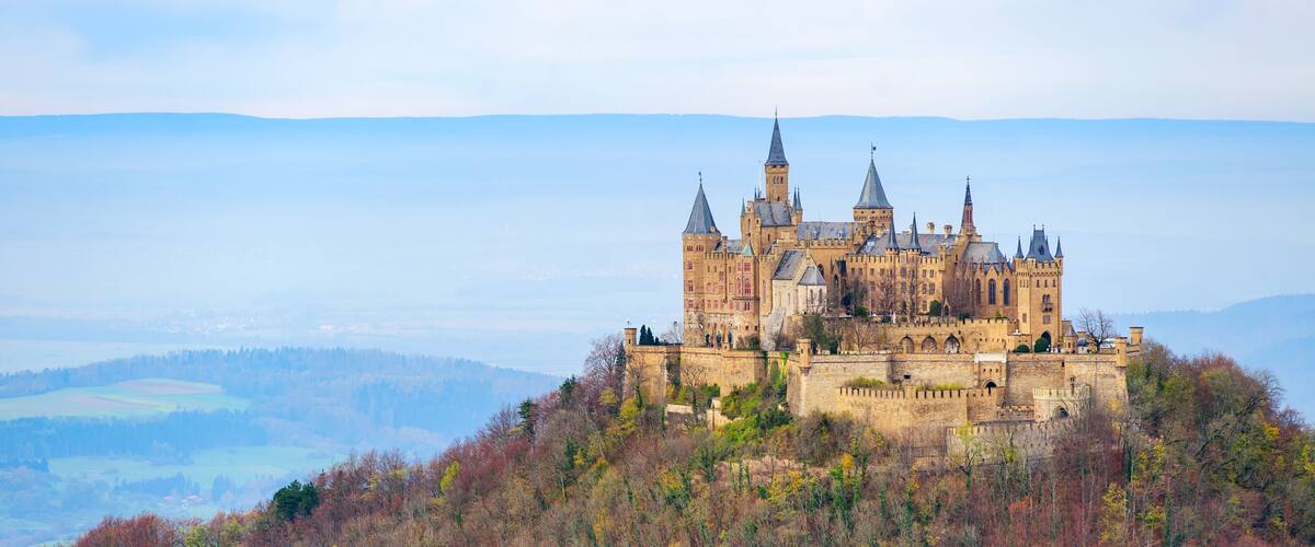 A historic castle on a hill surrounded by autumn-colored trees.