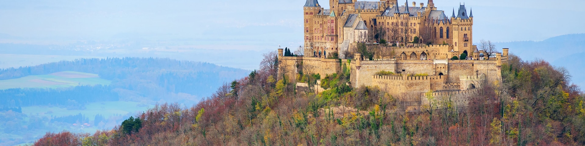 A historic castle on a hill surrounded by autumn-colored trees.