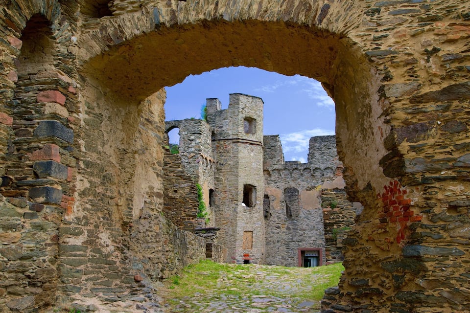 Un antiguo arco de piedra que conduce a un castillo medieval, con ruinas visibles y un camino adoquinado.