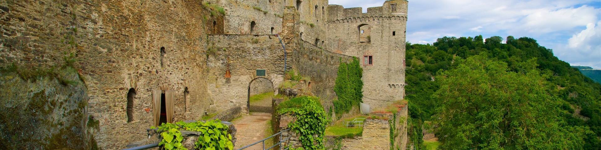 A historic stone castle with a steep, grassy hill behind it.