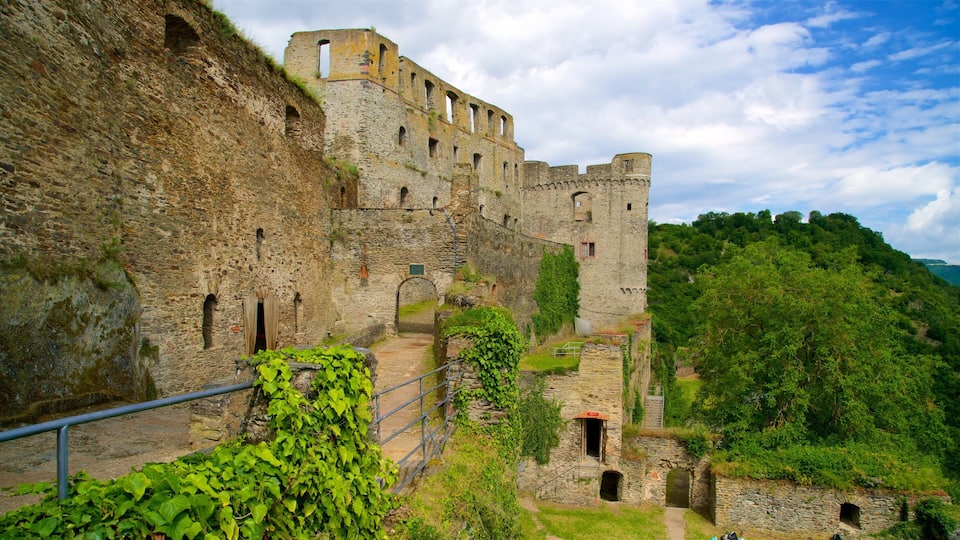 A historic stone castle with a steep, grassy hill behind it.