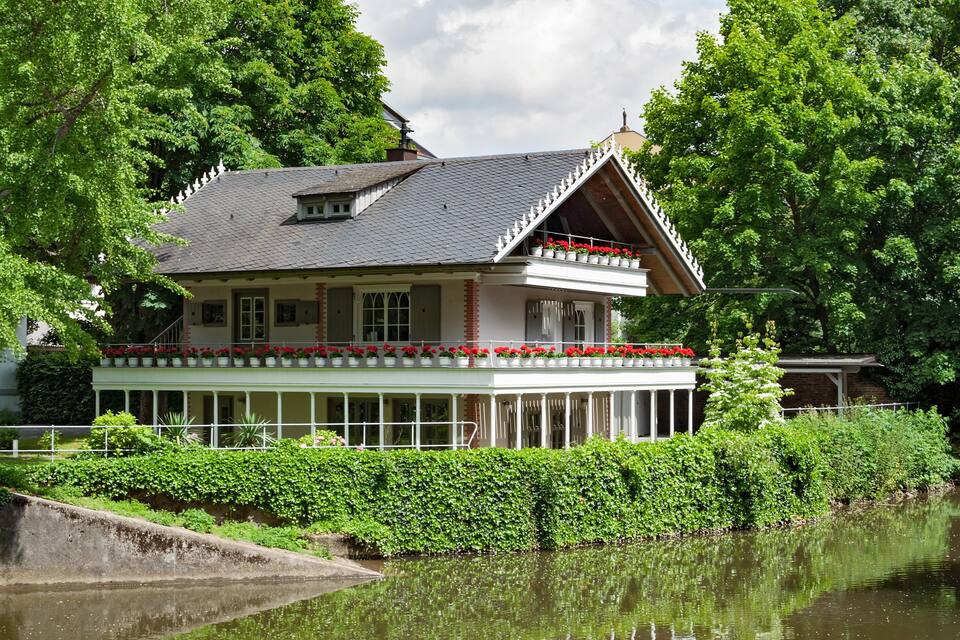 Une maison dotée d’un balcon, entourée d’une végétation luxuriante et bordée par un plan d’eau.