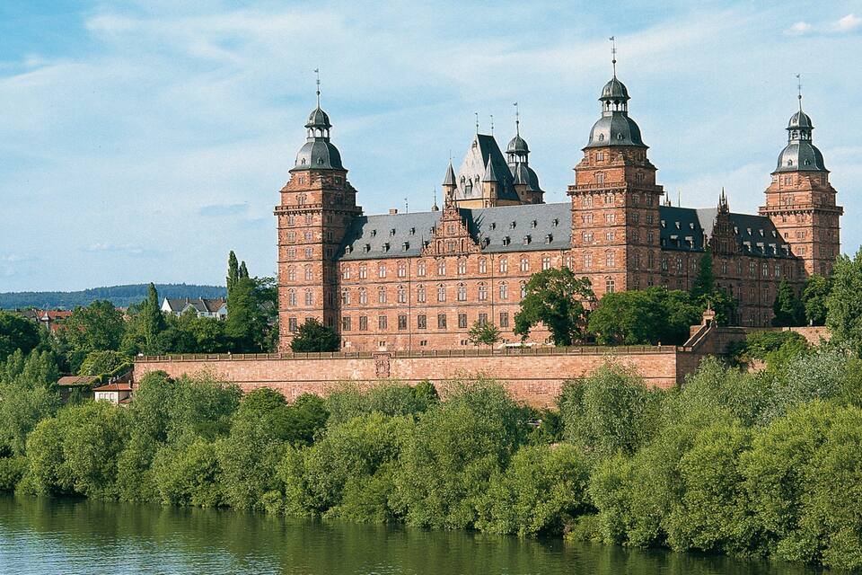 A large, historic building with multiple towers and a river in the foreground.