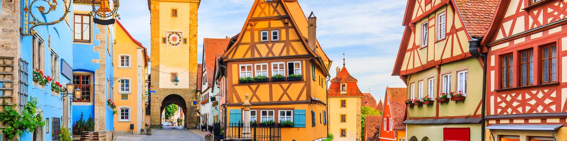 A cobblestone street lined with colorful half-timbered buildings, a church tower, and a clear blue sky.
