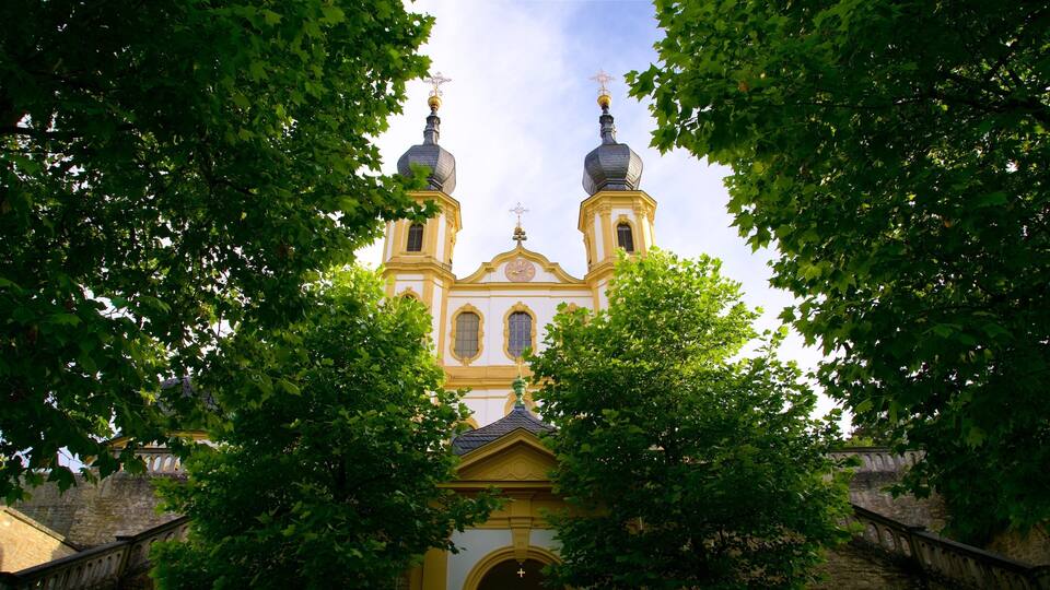 A church with two domes and a clock, surrounded by trees.