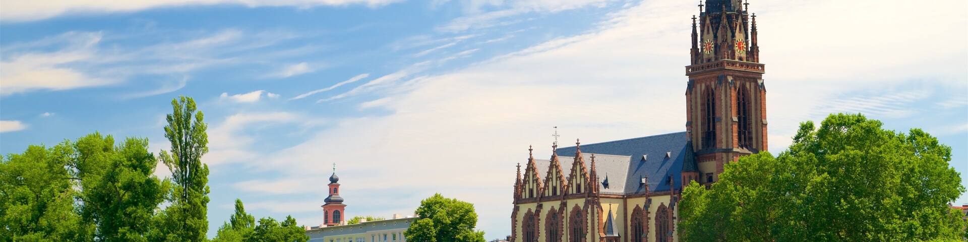 A historic church with a tall spire, surrounded by lush green trees and a calm river.