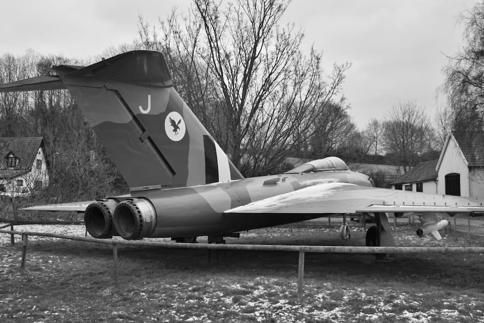 Un avion militaire exposé, peint avec un motif de camouflage, doté d’une dérive ornée d’un emblème représentant un oiseau et d’une hélice.