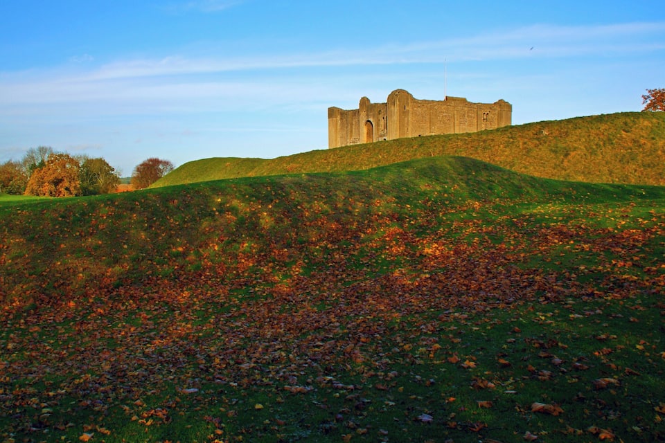 A historic castle on a grassy hill with autumn leaves.