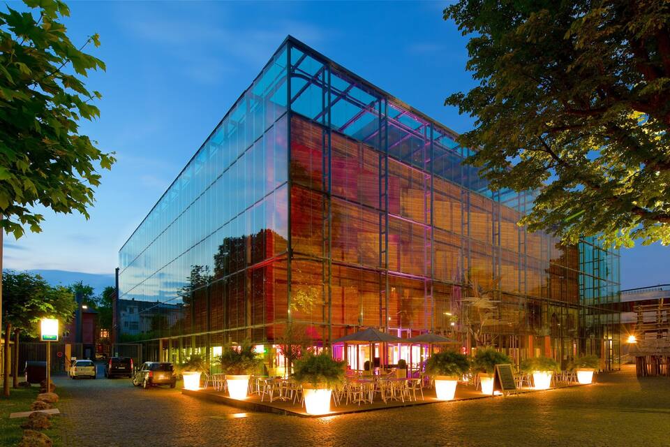 Un edifici modern de vidre amb seients a l'exterior i arbres.