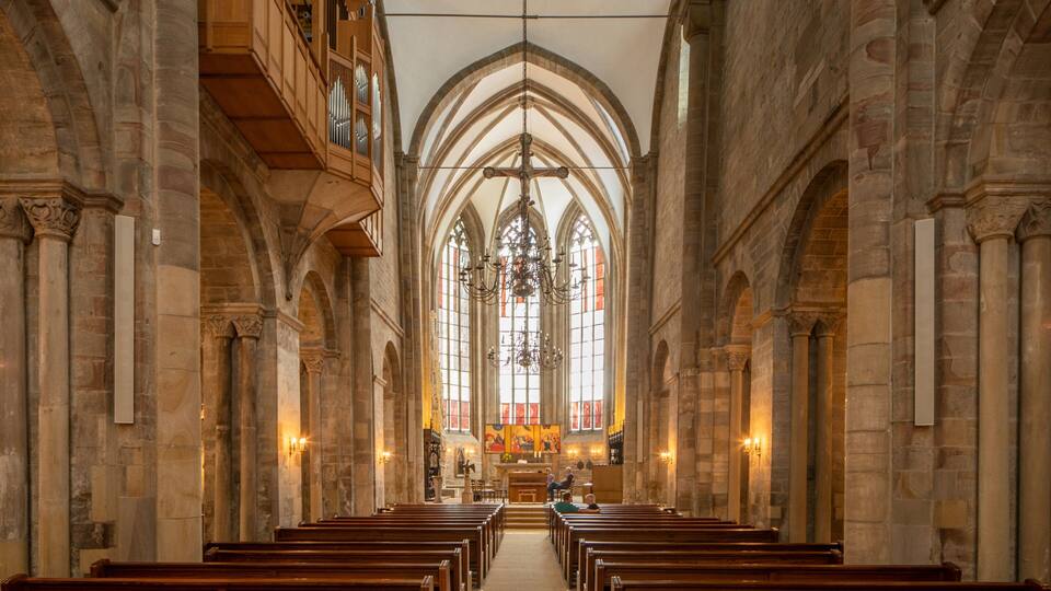 A church interior with arched ceilings, wooden pews, and stained glass windows.