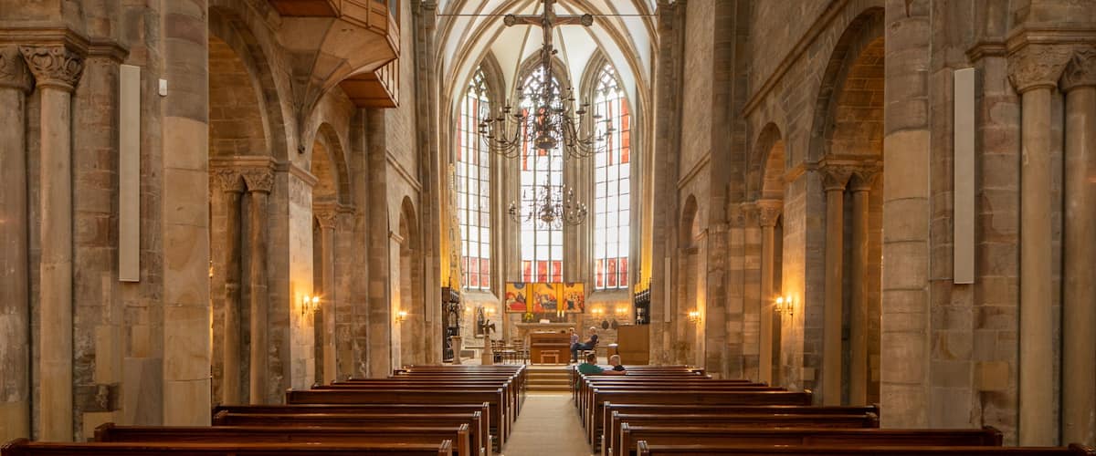 A church interior with arched ceilings, wooden pews, and stained glass windows.