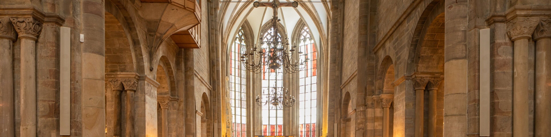 A church interior with arched ceilings, wooden pews, and stained glass windows.