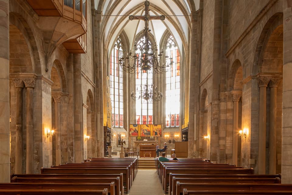 A church interior with high vaulted ceilings, wooden pews, and a central altar.