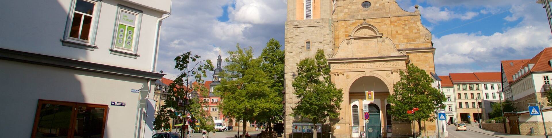 A historic church with a tall clock tower, surrounded by European-style buildings and trees.