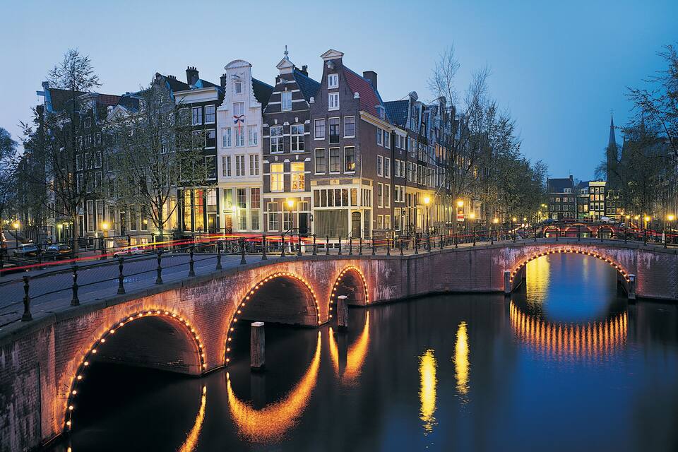 Um canal com uma ponte, arcos iluminados e edifícios históricos ao longo da água.