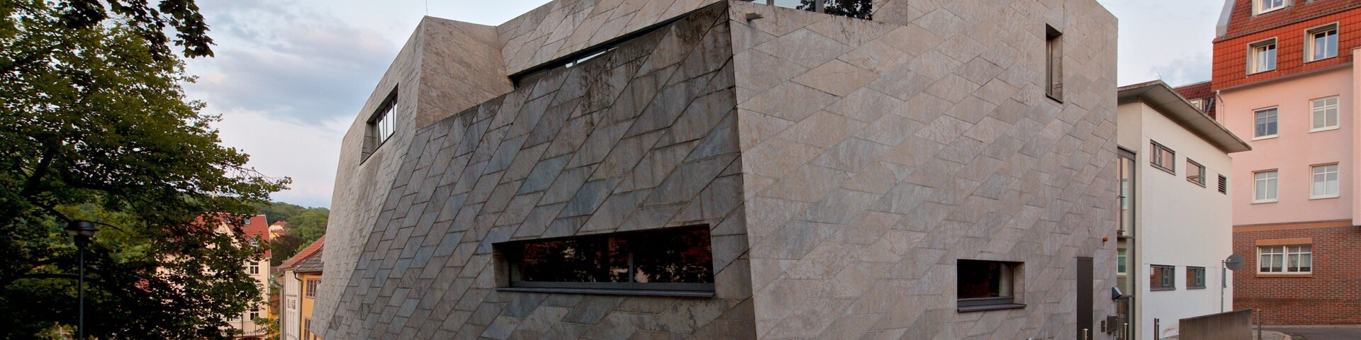 Un edificio moderno con una fachada geométrica única, rodeado de calles empedradas y edificios tradicionales.