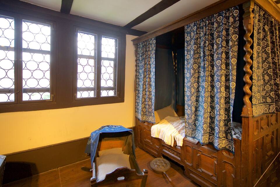 A traditional wooden bed with a canopy, a small stool, and a window with a geometric pattern.