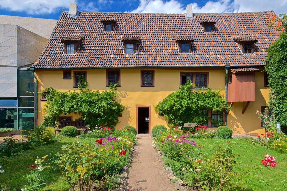 Une maison jaune avec un toit en tuiles et un jardin où poussent différentes sortes de fleurs.