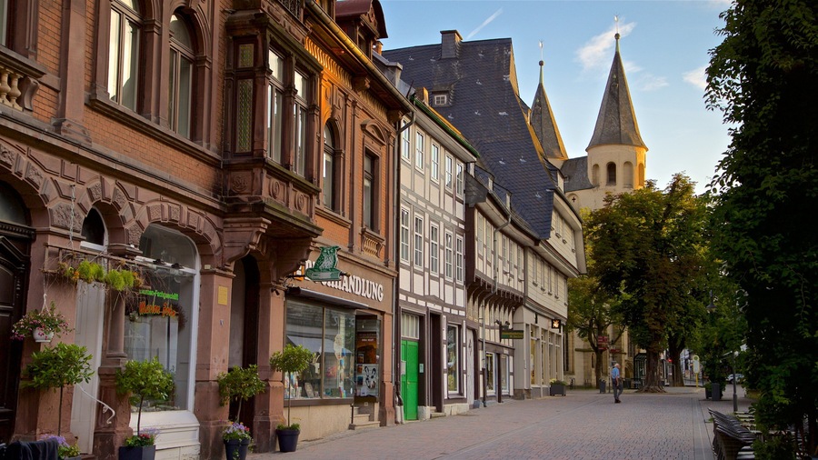 Eine Kopfsteinpflasterstraße gesäumt von historischen Gebäuden, einem Kirchturm und Kübelpflanzen.
