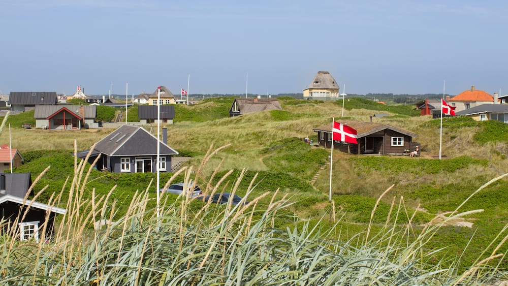 Danish holiday houses scattered among the sand dunes at the North Sea coastline in Soendervig, Denmark. Picture taken on a sunny summer day. Danish flags are visible on the picture.