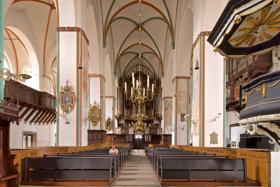 An ornate church interior with high vaulted ceilings, rows of pews, and elaborate chandeliers.