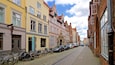 Eine Kopfsteinpflasterstraße gesäumt von historischen Gebäuden, mit abgestellten Fahrrädern und Autos.
